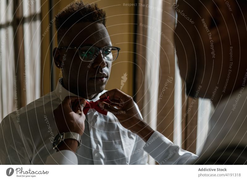 Ethnische Brüder in stilvollen Outfits im Zimmer am Hochzeitstag striegeln ausrichten Fliege Bruder Trauzeuge Hilfsbereitschaft Freund Jungvermählter Verlobter