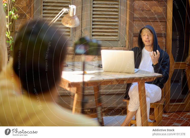 Unbekannter Fotograf und Vlogger im Gespräch im Innenhof Laptop Video Aufzeichnen Fotoapparat sprechen soziale Netzwerke gestikulieren Männer patio Netbook