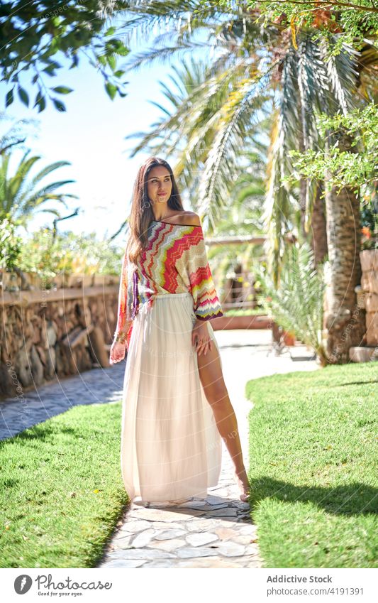 Junge Frau in modischer Sommerkleidung steht im Hof eines tropischen Gartens Mode Stil Barfuß Model Kleidungsstück selbstbewusst Outfit anhaben jung ethnisch