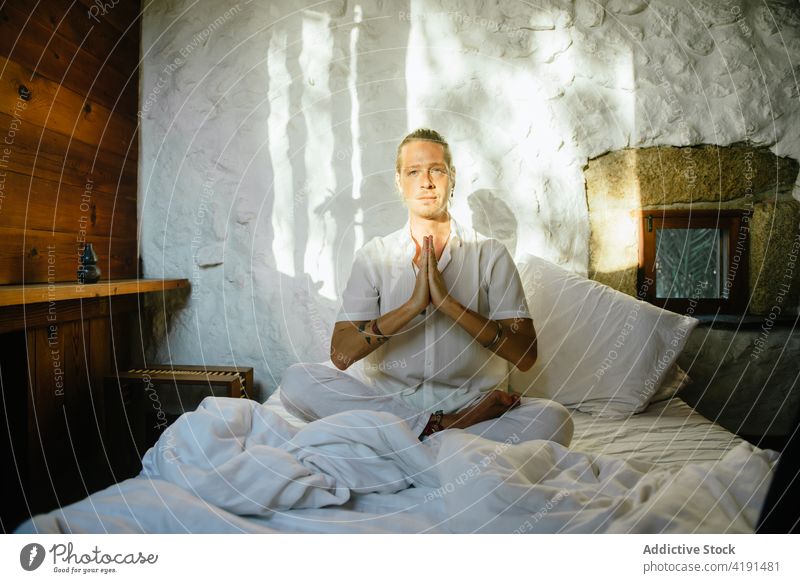 Blonder Mann sitzt auf einem Bett und praktiziert Meditation blond Sitzen Schlafzimmer Yoga Dehnung Flexibilität Wellness Gesundheit Übung Sportbekleidung