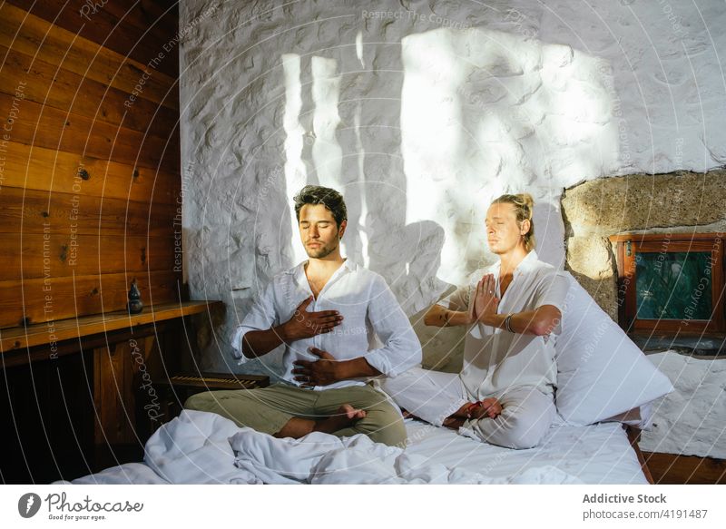 Zwei Freunde sitzen auf einem Bett und üben sich in Meditation Paar Mann blond Sitzen Schlafzimmer Yoga Dehnung Flexibilität Wellness Männer Gesundheit Übung