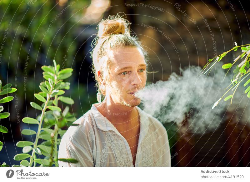 Hipster blonder Mann raucht Zigarette im Garten männlich gutaussehend Stil selbstsicher im Freien Sommer Harmonie idyllisch Windstille ruhig Hippie Gelassenheit