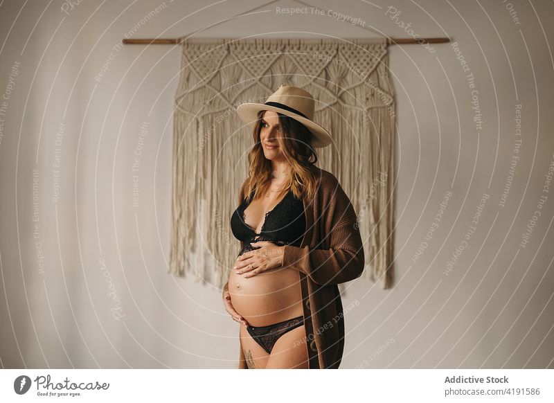 Schwangere Frau, die ihren Bauch berührt und wegschaut schwanger Lächeln Glück besinnlich Stil Bauch anfassen Mutterschaft pränatal erwarten Appartement Dessous