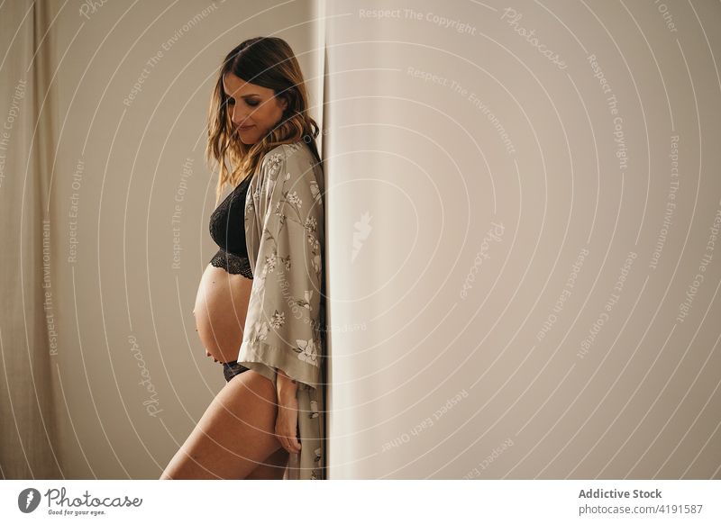 Schwangere Frau, die ihren Bauch berührt und nach unten schaut schwanger besinnlich Stil Bauch anfassen Textfreiraum Dessous Bademantel Mutterschaft pränatal