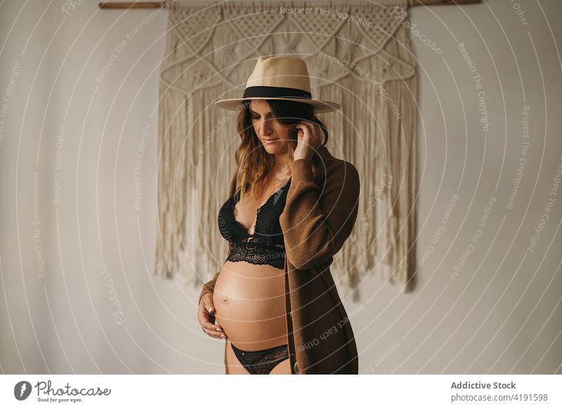Schwangere Frau, die ihren Bauch berührt und nach unten schaut schwanger besinnlich Stil Bauch anfassen Mutterschaft pränatal erwarten Appartement Dessous Hut