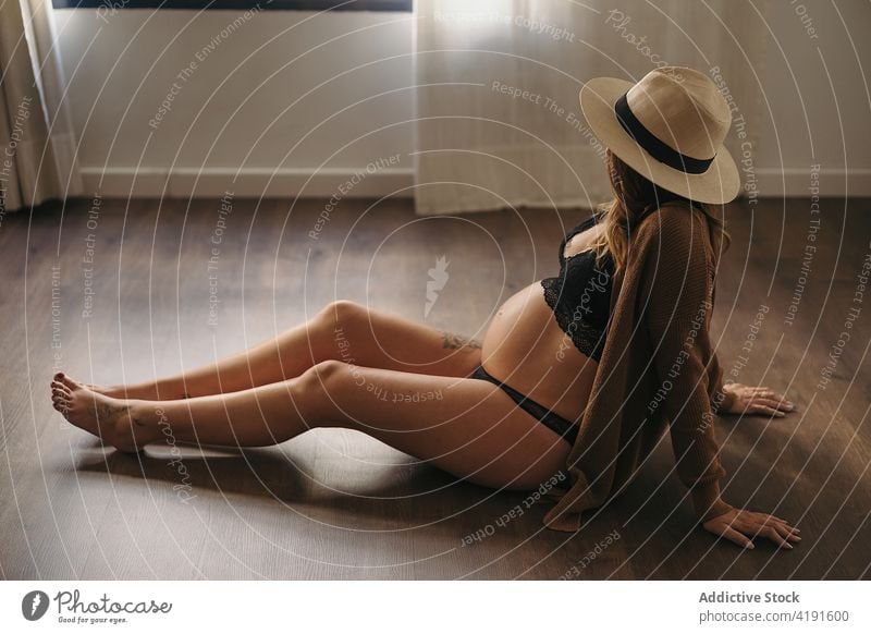 Anonyme schwangere Frau auf dem Boden sitzend anonym besinnlich Schwangerschaft entspannt mütterlich erwarten aussruhen Kühlung Stil Mutter Bauch anfassen Hut