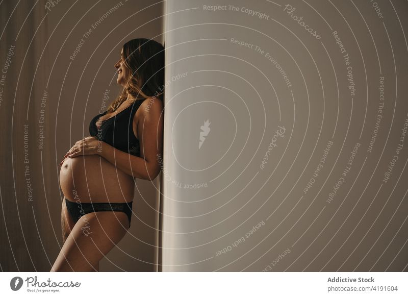 Schwangere Frau in Unterwäsche steht im Raum und schaut weg schwanger mütterlich Dessous Mutter erwarten pränatal Appartement heiter Mutterschaft
