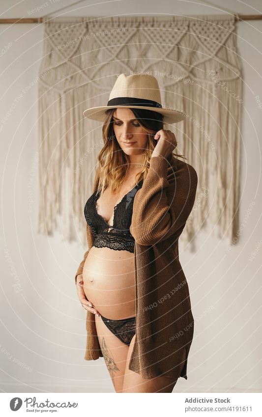 Schwangere Frau, die ihren Bauch berührt und nach unten schaut schwanger besinnlich Stil Bauch anfassen Mutterschaft pränatal erwarten Appartement Dessous Hut