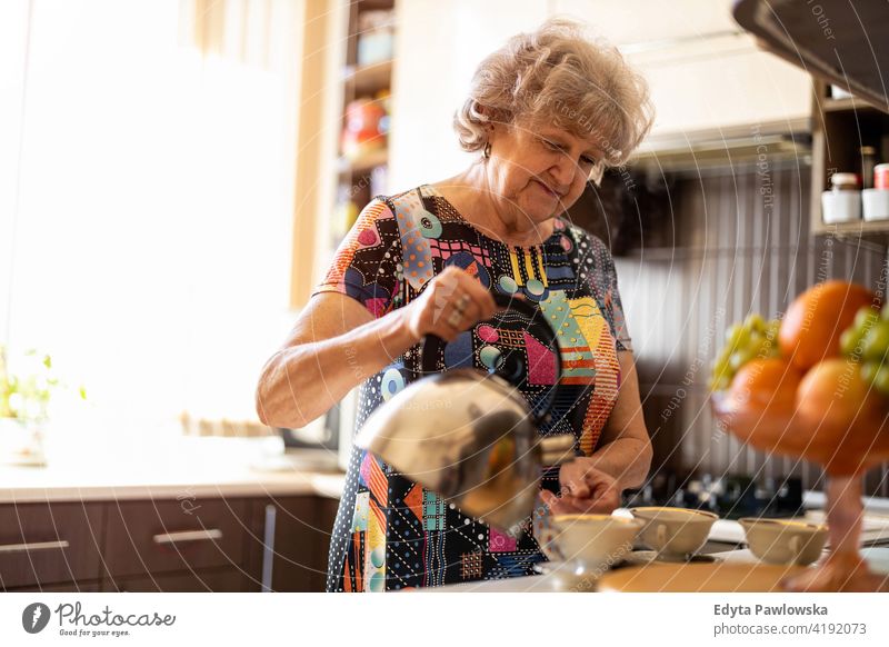 Ältere Frau mit Wasserkocher gießt heißes Wasser in Tasse in der Küche vorbereitend Tee trinken Frühstück Kaffeetasse Herstellung Koffein Gießen Wasserkessel