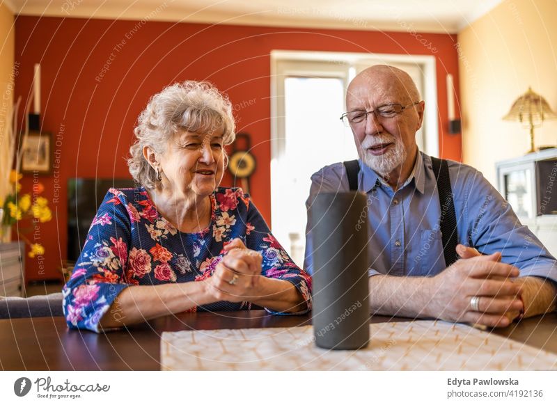 Älteres Paar schaut aufgeregt, während es mit einem interaktiven Sprachassistenten Smart Speaker echte Menschen offen Frau Senior reif männlich Mann