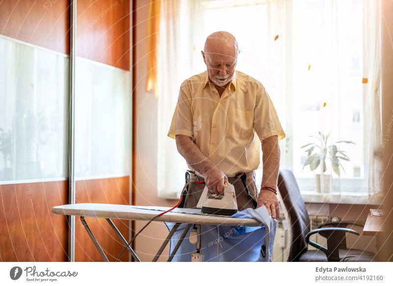Senior Mann zu Hause bügeln seine Kleidung echte Menschen offen reif männlich Kaukasier älter heimwärts alt Alterung häusliches Leben Großvater Rentnerin