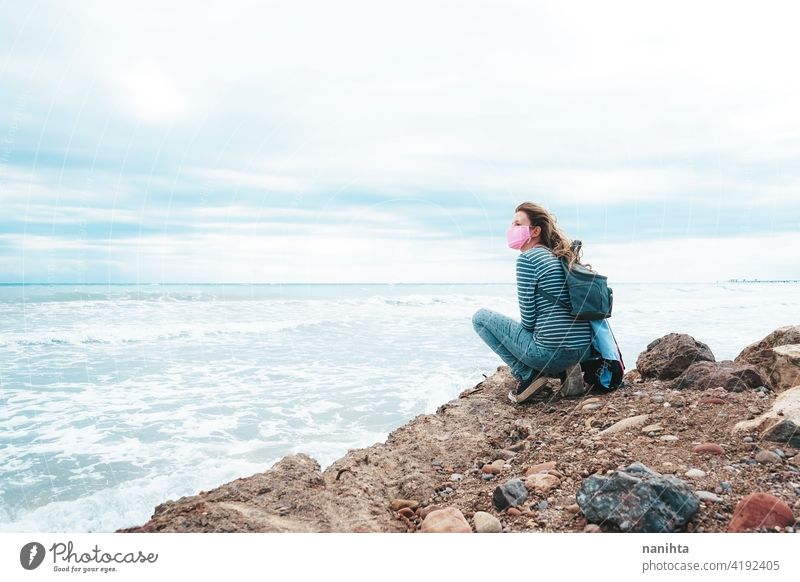 Junge Frau trägt eine rosa Gesichtsmaske sitzt in der Nähe des Meeres Hoffnung Mut stark COVID Coronavirus Strand MEER ocecan frei Freiheit Mundschutz