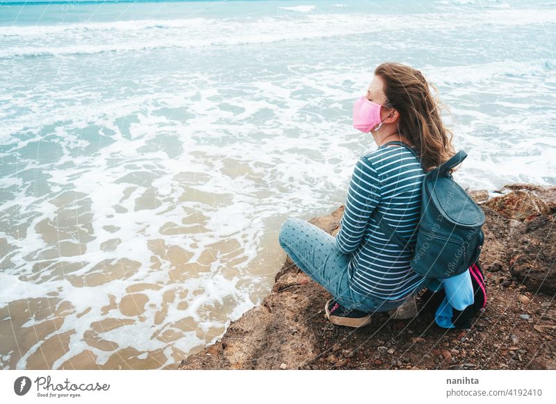 Junge Frau trägt eine rosa Gesichtsmaske sitzt in der Nähe des Meeres Hoffnung Mut stark COVID Coronavirus Strand MEER ocecan frei Freiheit Mundschutz