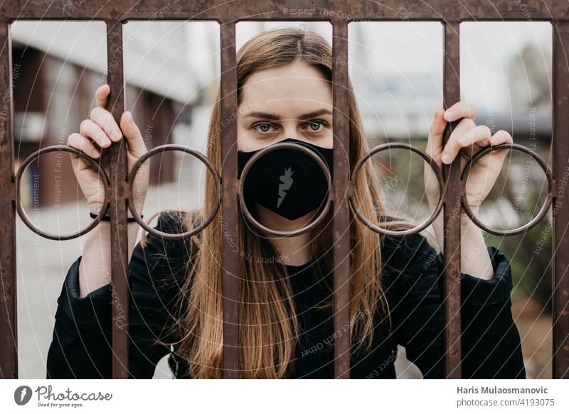 Frau mit Gesichtsmaske hinter den Gittern im Freien, Konzept Lockdown Covid 19 Erwachsener allein Käfig Korona Corona-Virus Coronavirus COVID Covid-Sperre