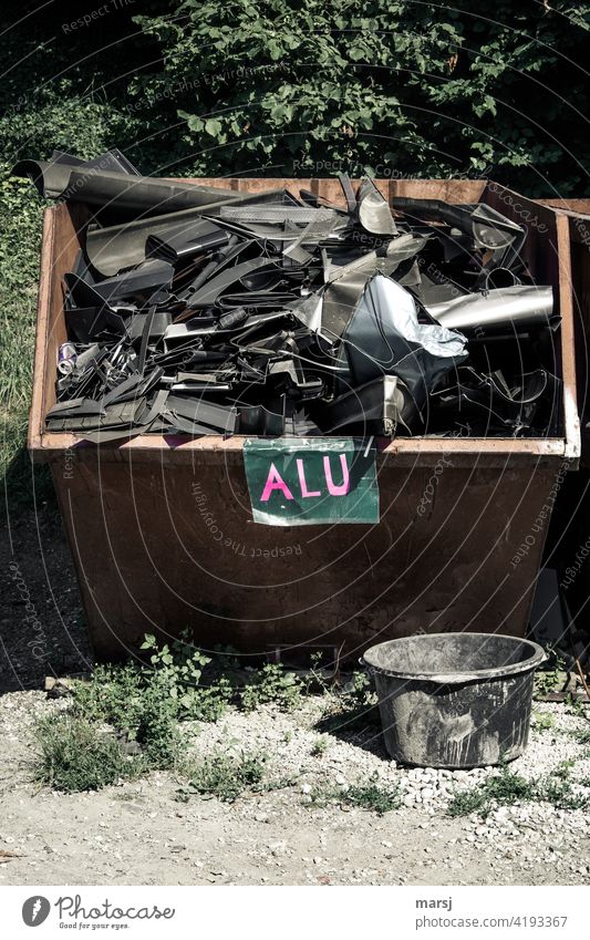 ALU. Gut gefüllter Alu-Schrottcontainer. Runde Mörtelwanne im Vordergrund. Rohstoffe nachhaltige Ressourcen Buchstaben Beschriftung Umweltschutz