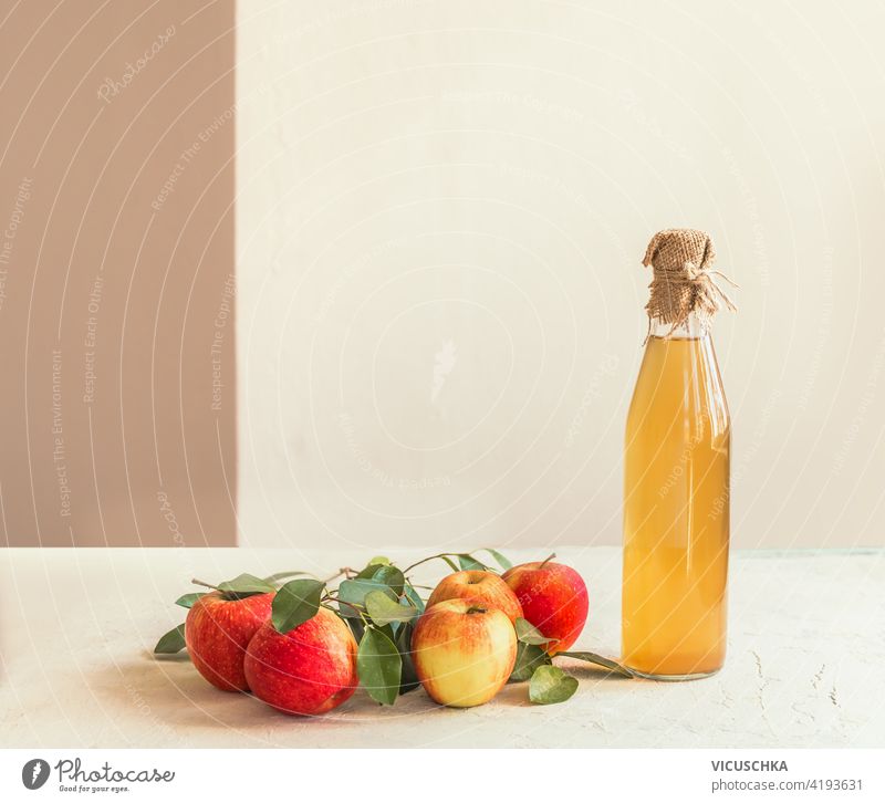 Flasche mit hausgemachtem Apfelessig mit frischen Äpfeln und grünen Blättern auf weißem Küchentisch. Stilleben Saft Essig selbstgemacht Tisch Stillleben