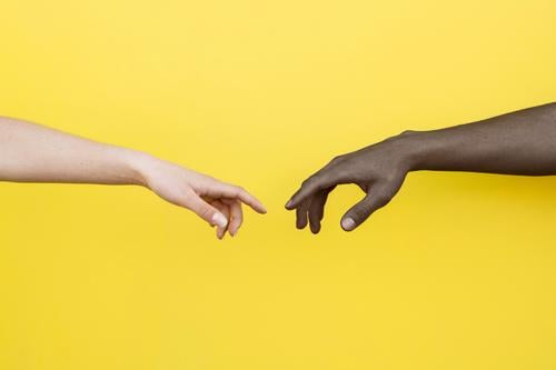 Weiße Hand und schwarze Hand über zu berühren auf gelbem Hintergrund Menschen Freundschaft Zusammensein umklammert Afrikanisch international Partnerschaft Haut