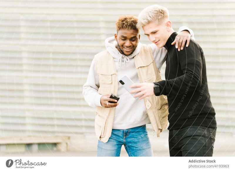 Positive junge männliche Freunde teilen sich auf der Straße ein Smartphone Männer Lächeln Glück Zusammensein soziale Netzwerke zeigen Video Mobile Telefon