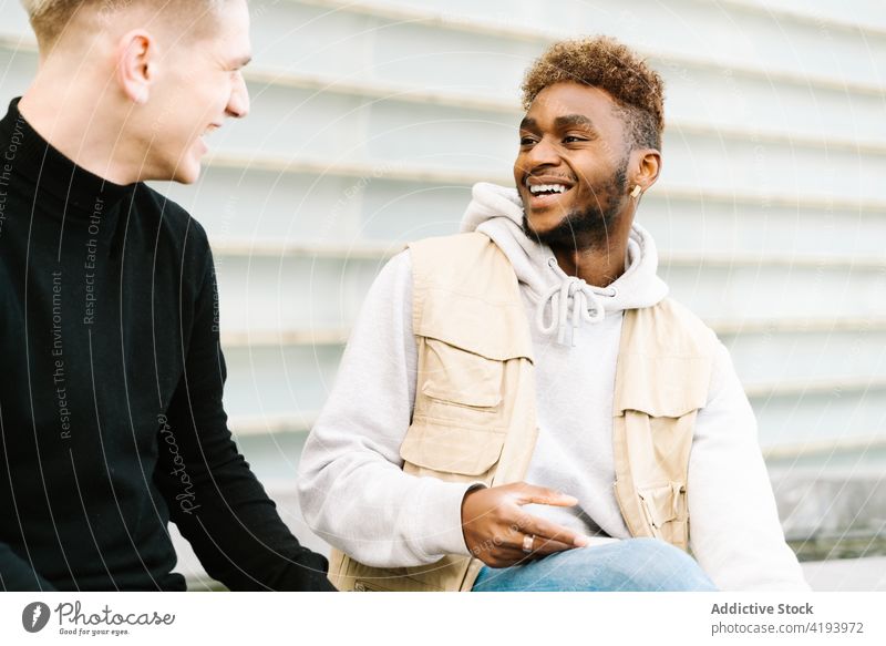 Positiv eingestellte junge Männer, die auf dem Bürgersteig im Stadtviertel stehen und lächeln Lächeln Zusammensein Freund Großstadt Straße urban Gebäude