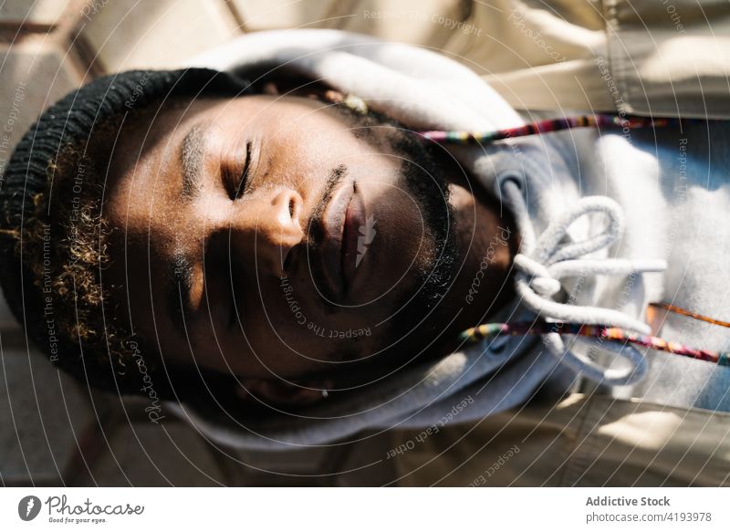 Junger Schwarzer schläft auf der Straße im Sonnenlicht Mann schlafen Augen geschlossen Windstille Erholung Großstadt Boden Lügen trendy Harmonie ruhig männlich