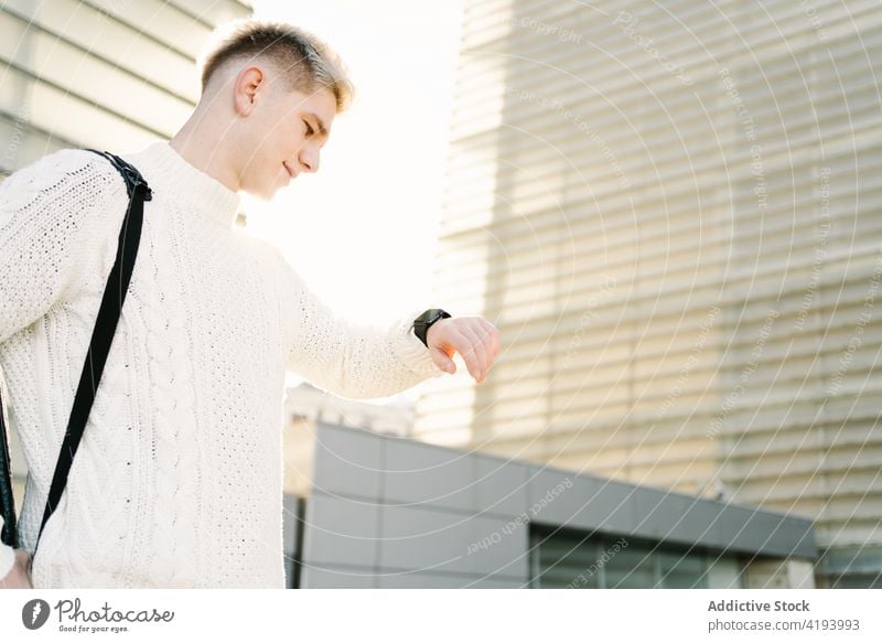 Trendiger junger Mann, der die Zeit auf seiner Armbanduhr überprüft, während er in der Nähe moderner Gebäude steht prüfen Straße Großstadt warten Ernennung