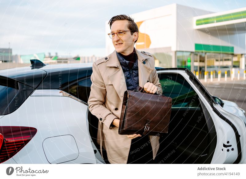 Lächelnder Geschäftsmann mit Aktenkoffer beim Aussteigen aus dem Auto PKW Automobil Unternehmer Verkehr gutaussehend Manager selbstbewusst männlich Mann Mantel