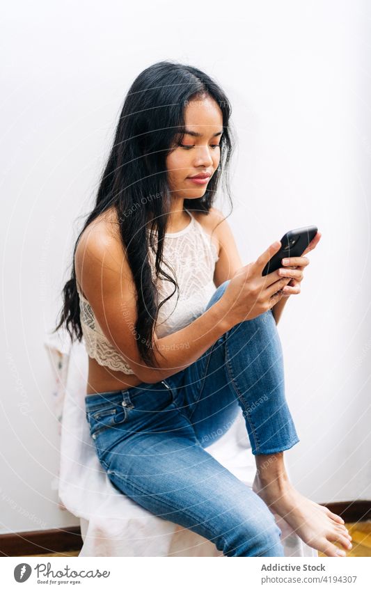 Langhaarige asiatische Frau, die zu Hause sitzt und ein Mobiltelefon benutzt Japanisch Asien jung Model brünett Chinesisch Stil heimwärts Sitzen Telefon