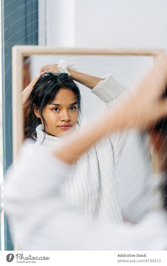 Langhaarige brünette Asiatin im weißen Pullover, die in den Spiegel schaut und sich die Haare kämmt Japanisch Frau asiatisch Asien jung Model Chinesisch Stil