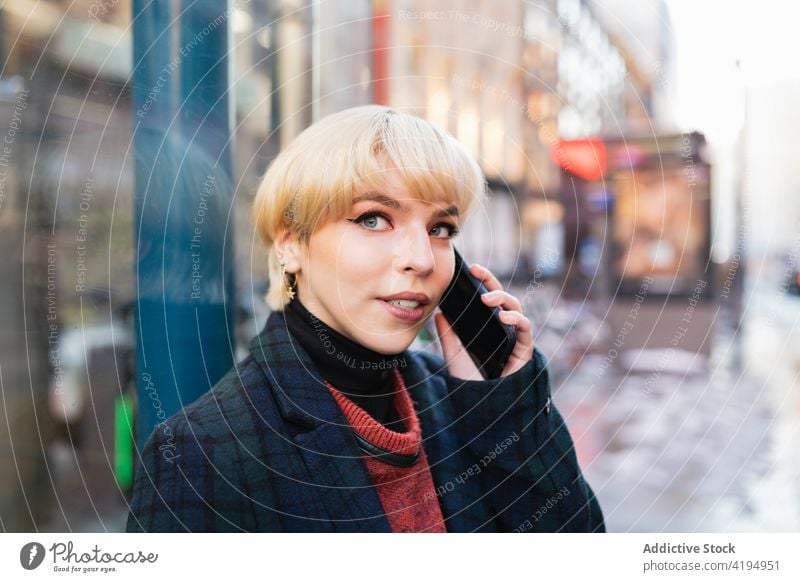 Attraktive junge Frau, die auf der Straße mit ihrem Smartphone spricht reden Telefonanruf positiv Anruf Saison diskutieren Gespräch Großstadt Kommunizieren