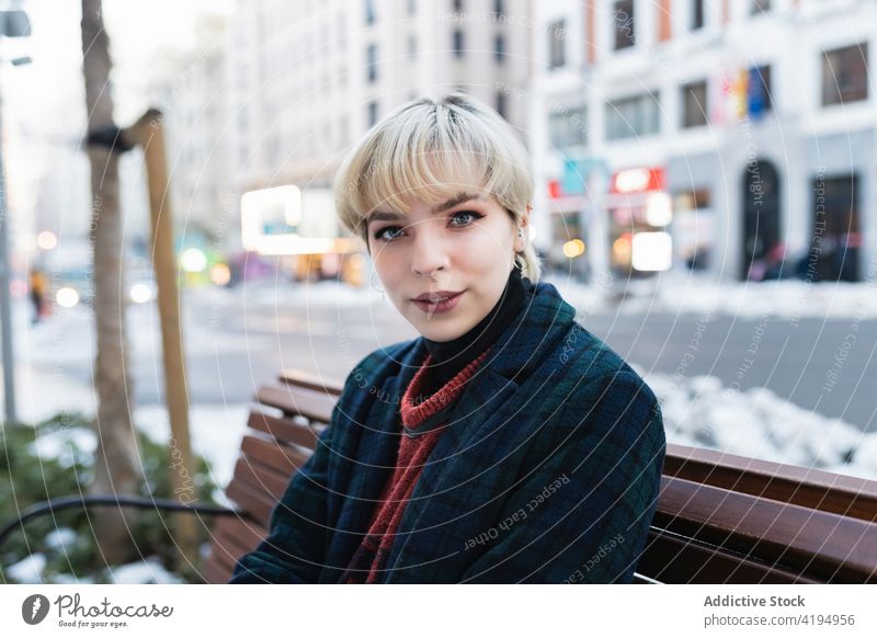 Positive junge Frau, die sich auf einer Bank in einer modernen Stadt ausruht Straße Großstadt warme Kleidung Saison Herbst urban ruhen Stil schön trendy lässig