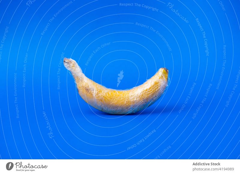 Frische Banane in Frischhaltefolie auf blauem Hintergrund Ackerbau Industrie Überbeanspruchung Kunststoff Konzept Frucht frisch reif geschmackvoll ganz Vitamin