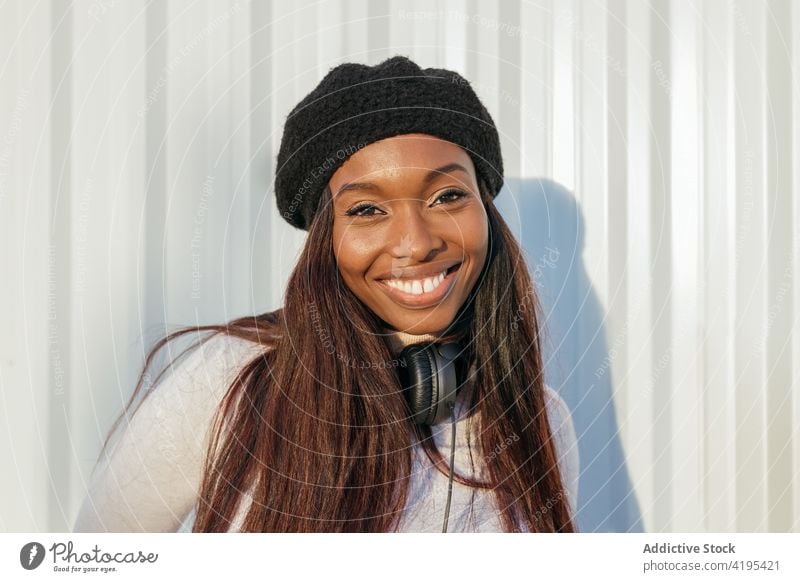 Charmante schwarze Frau schaut in der Stadt in die Kamera charmant Vorschein Lächeln Baskenmütze Großstadt Kopfhörer heiter Schönheit natürlich ethnisch