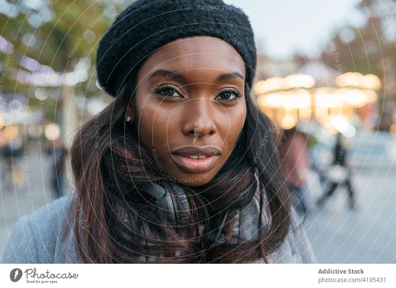 Lächelnde ethnische Frau genießt in der Stadt und schaut in die Kamera Kopfhörer genießen heiter Straße Gesang schwarz Afroamerikaner Inhalt Gerät Klang Melodie