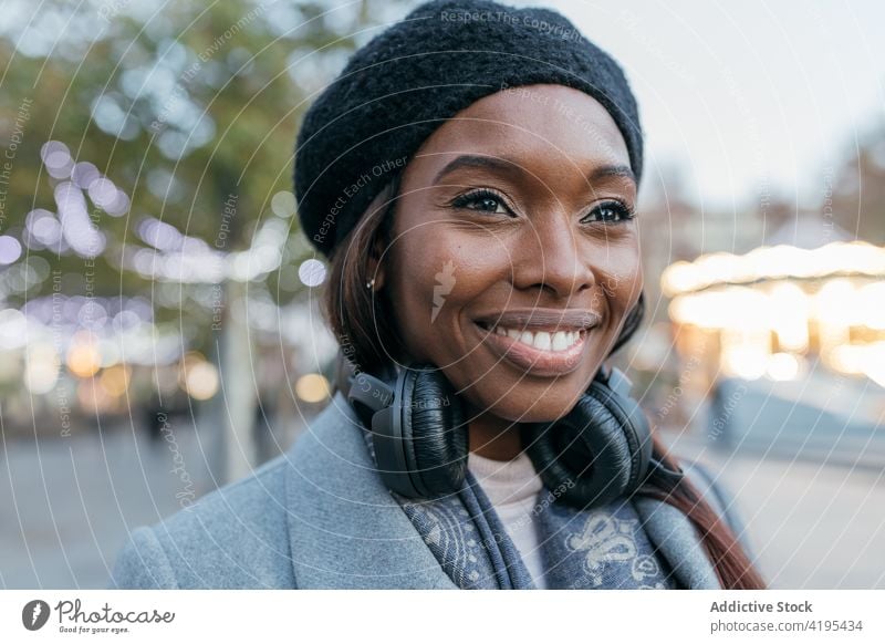 Lächelnde ethnische Frau, die in der Stadt genießt und wegschaut Kopfhörer genießen heiter Straße Gesang schwarz Afroamerikaner Inhalt Gerät Klang Melodie Glück