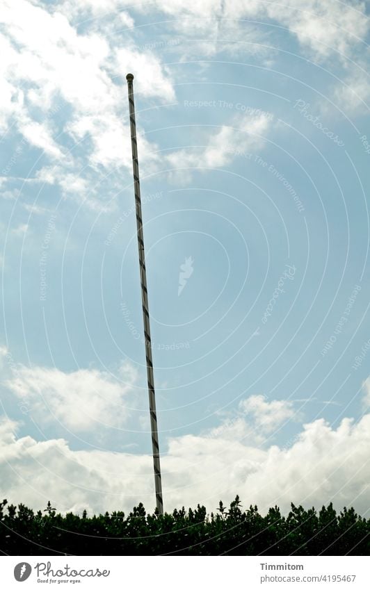 Eine Fahnenstange mit Schlagseite Flaggenstock verziert geschmückt schief Himmel Wolken schönes Wetter Gebüsch Grünzeug Außenaufnahme Menschenleer Tag Farbfoto