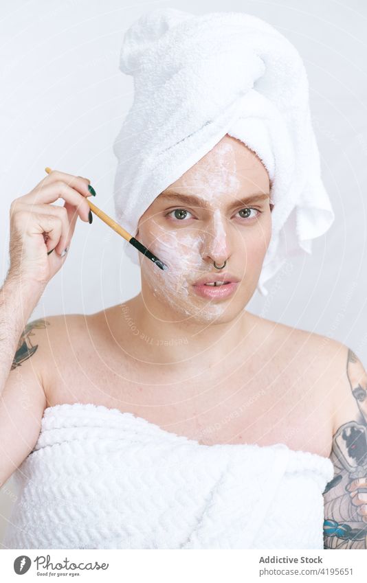 Gay trägt die Reinigungsmaske mit dem Applikator auf die Wange auf queer bewerben Mundschutz Schönheit Kosmetik Gesichtsbehandlung verträumt Porträt Mann