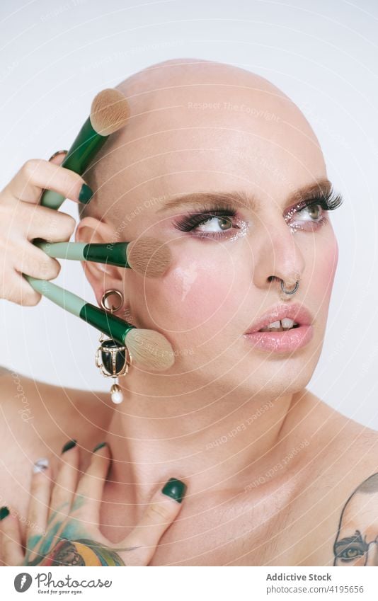 Queer mit verschiedenen Schminkpinseln auf weißem Hintergrund Transgender Mann Bürste Kosmetik Make-up Schönheit Tattoo feminin Werkzeug Porträt sortiert