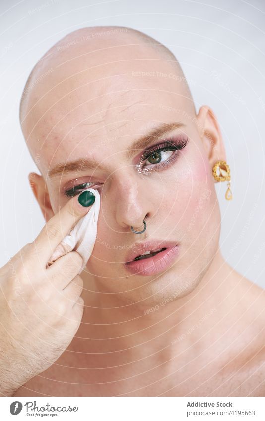 Androgyner Mann beim Abschminken der Augenlider auf weißem Hintergrund transsexuell entfernen Make-up Gesichtsbehandlung Kosmetik Schönheit Unterlage Porträt