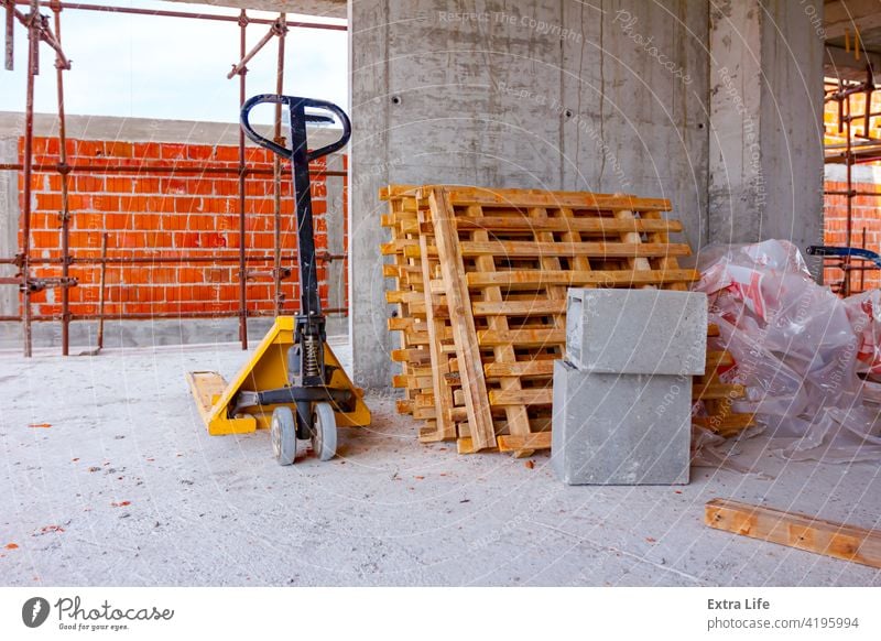 Deichselstapler und gestapelte Holzpaletten an der Wand im Hintergrund gegen Architektur angeordnet Klotz Baustelle Haufen Ladung führen Zement Tiefbau Beton