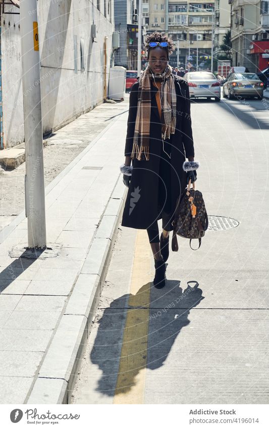 Stilvolle schwarze Frau geht auf der Straße mit Schatten stylisch Mode selbstbewusst feminin Accessoire Spaziergang freundlich herzlich Stadt Gebäude Großstadt