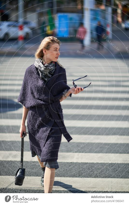 Stilvolle Frau beim Überqueren einer städtischen Straße stylisch fliegendes Haar schlendern Mode Stadt Lifestyle Sonnenbrille blond Zebrastreifen schwarz Stoff