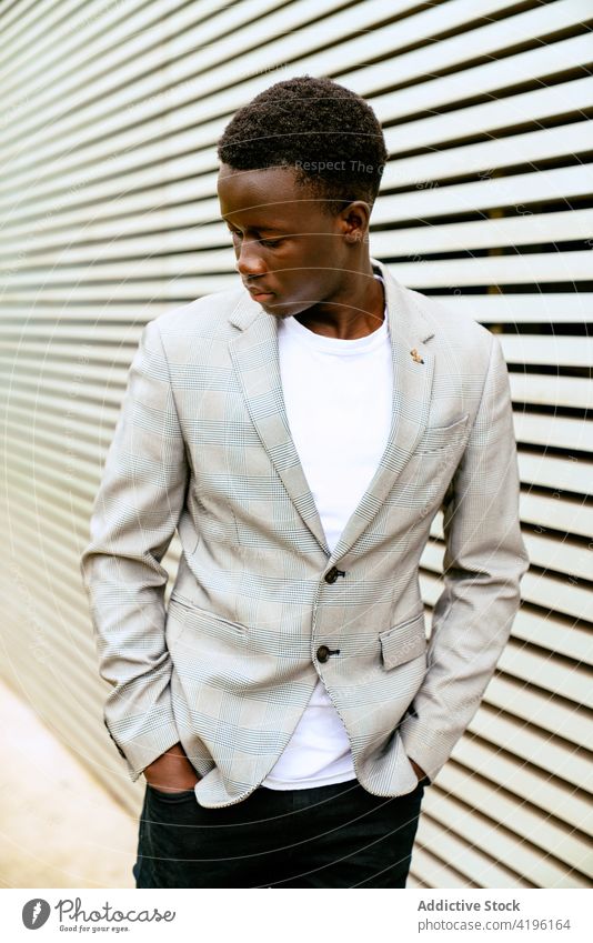Stilvoller schwarzer Mann auf städtischem Bürgersteig in der Nähe einer gerippten Wand stylisch Mode maskulin Macho achtsam Model auf Zehenspitzen Stadt trendy