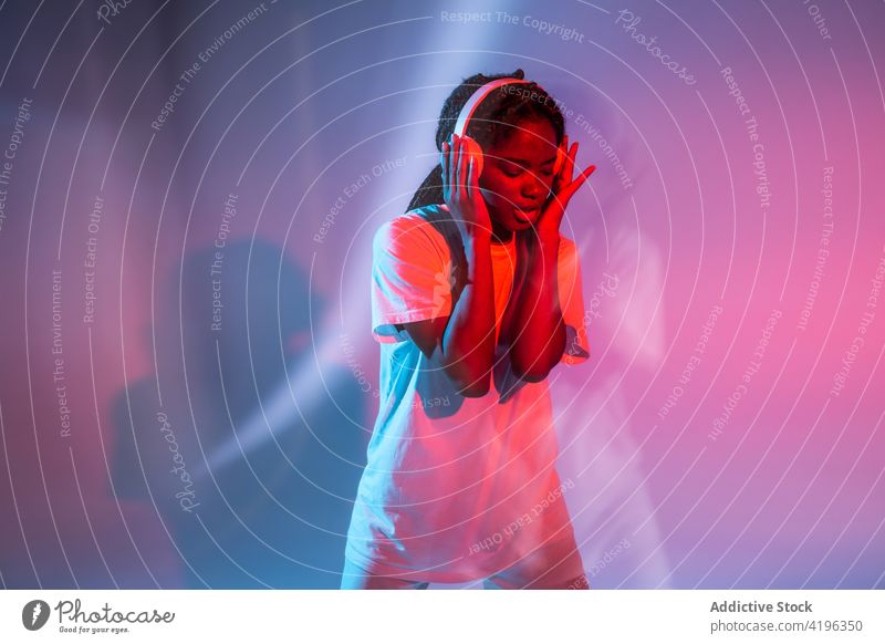 Ausdrucksstarkes schwarzes Teenager-Mädchen, das mit drahtlosen Kopfhörern Musik hört zuhören genießen expressiv Gesang neonfarbig Wiedergabeliste unterhalten