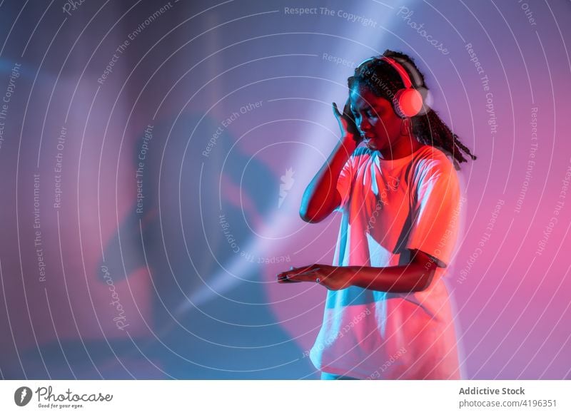 Ausdrucksstarkes schwarzes Teenager-Mädchen, das mit drahtlosen Kopfhörern Musik hört zuhören genießen expressiv Gesang neonfarbig Wiedergabeliste unterhalten