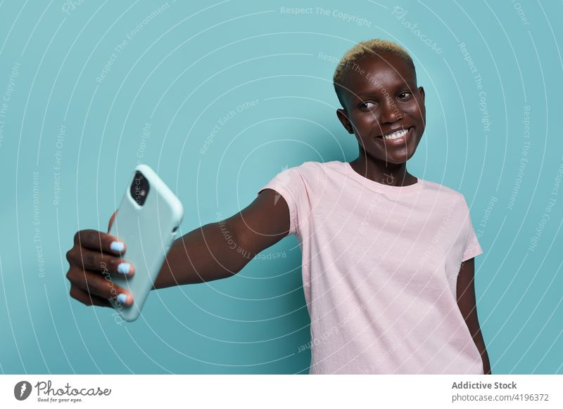 Fröhliche schwarze Frau macht Selfie im Studio Smartphone expressiv Afrikanisch trendy feminin fotografieren Moment Studioaufnahme Zahnfarbenes Lächeln Mobile