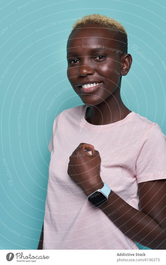 Fröhliche schwarze Frau mit Smartwatch im Studio intelligente Uhr Zahnfarbenes Lächeln Model charismatisch trendy heiter zeigen manifestieren Stil Gerät