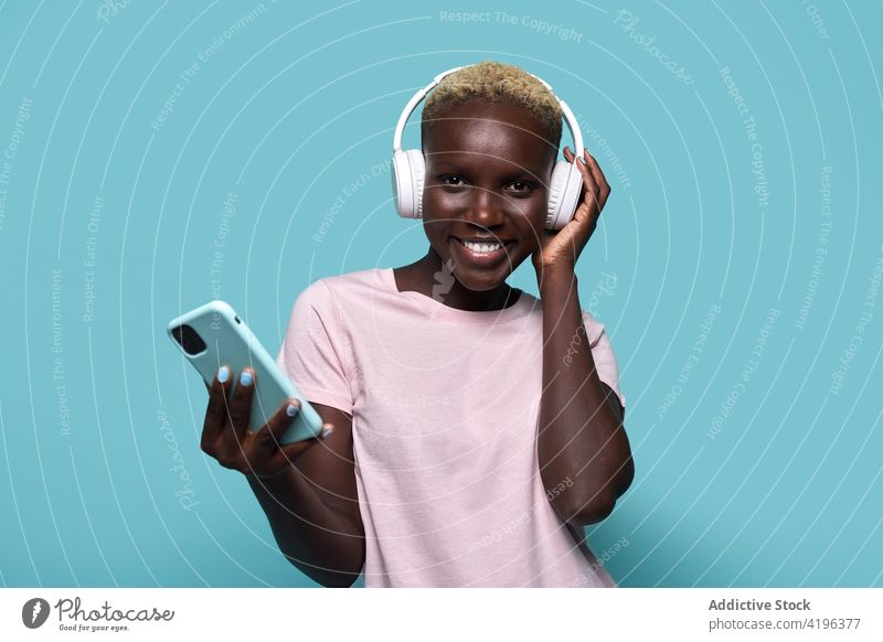 Aufgeregte schwarze Frau mit Kopfhörern und Smartphone Musik Afrikanisch charismatisch expressiv Audio Gerät Gesang Apparatur froh Amerikaner Handy Melodie