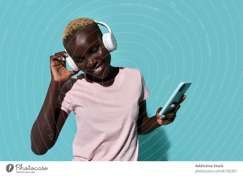Aufgeregte schwarze Frau mit Kopfhörern und Smartphone Musik Tanzen Afrikanisch charismatisch expressiv Audio Gerät Gesang Apparatur froh Amerikaner Handy