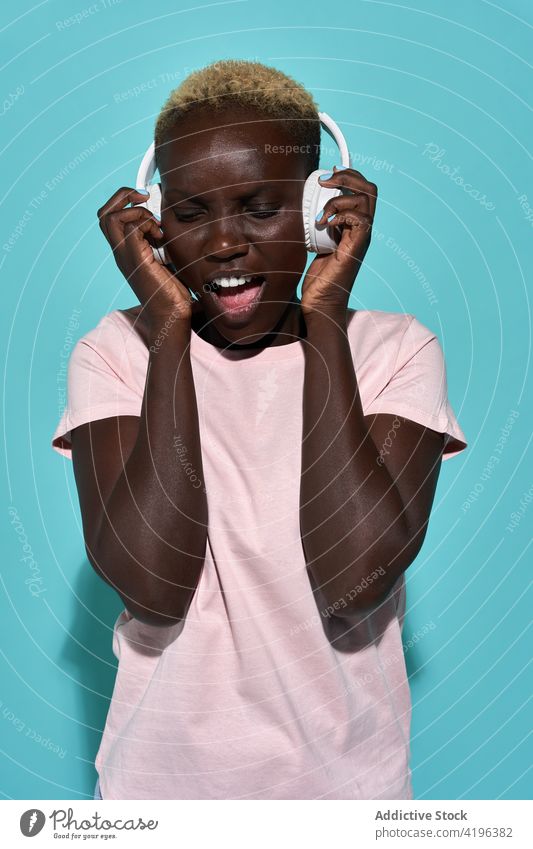 Aufgeregte schwarze Frau mit Kopfhörern Musik Afrikanisch charismatisch expressiv singen Audio Gerät Kurze Haare Gesang Apparatur genießen froh Amerikaner