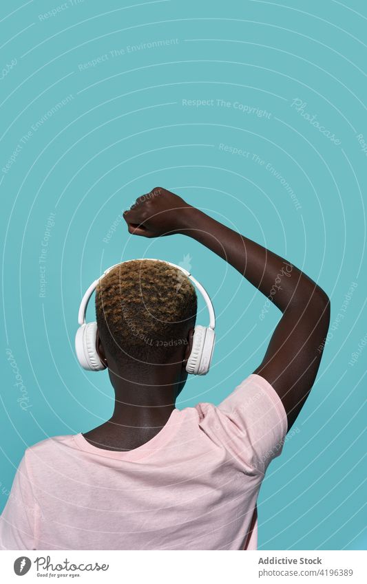 Schwarze Frau mit Kopfhörern und erhobenem Arm Arm angehoben Studioaufnahme zuhören Musik Audio Melodie Stil Apparatur Gerät Klang Faust geschlossen